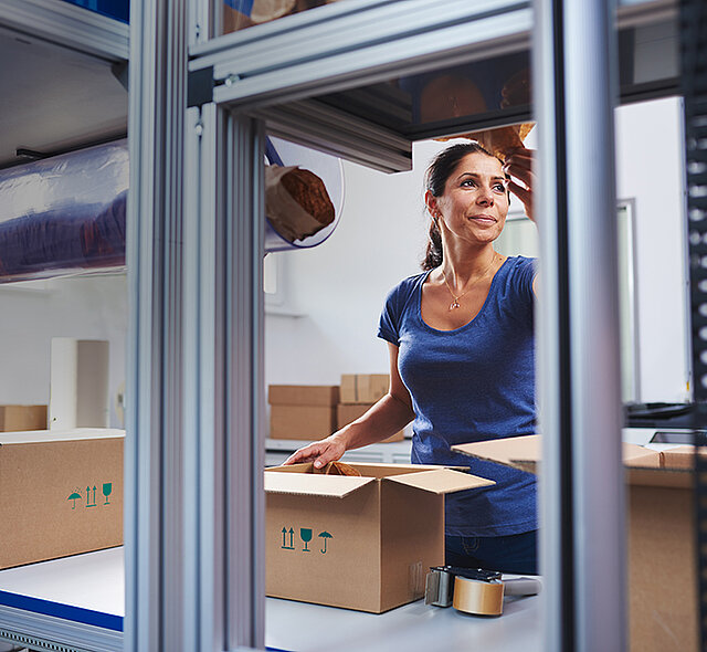 
			Une femme emballant des produits dans une boîte en carton à une station d’emballage 